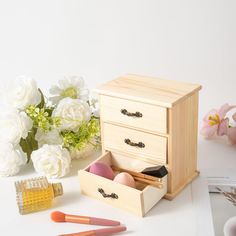 an open drawer with makeup and other items on it next to white flowers in vases