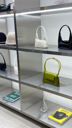 several purses and hats are on display in a glass case with metal shelves behind them