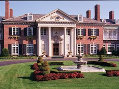 a large red brick building surrounded by lush green grass and shrubs with fountain in front