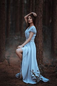 a woman in a blue dress leaning against a tree