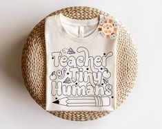 a t - shirt that says teacher of tiny humans on it next to a flower