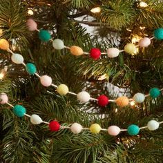 a christmas tree decorated with multicolored pom - poms and string lights