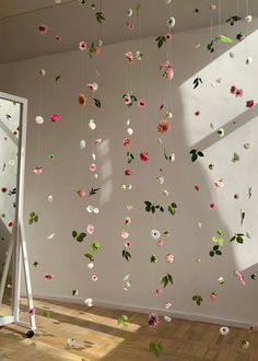 a white room with flowers hanging from it's ceiling and a mirror in the corner