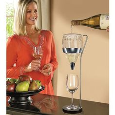 a woman pouring wine into a glass on top of a counter next to a plate of fruit