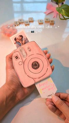 a person holding up a pink camera with a card in front of it that says happy mother's day