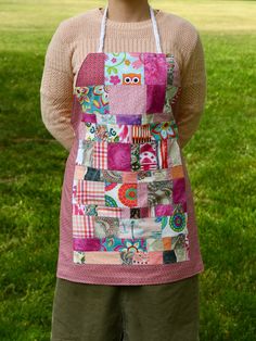 a woman wearing an apron made out of patchwork and fabric, standing in the grass