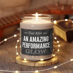 an amazing performance glow candle sits on a table next to a guitar and string lights