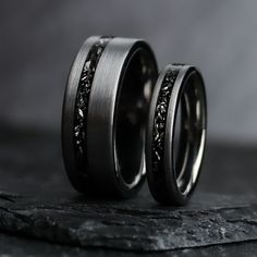 two wedding bands with black diamonds in them on top of a stone slabd surface