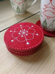 two red coasters sitting on top of a wooden table next to coffee mugs