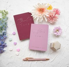 two pink notebooks with writing on them next to some flowers and other items that are scattered around