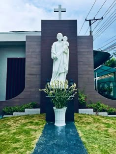 a large white statue sitting in the middle of a lush green field next to a building