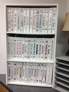 a white book shelf filled with books on top of a counter next to a lamp