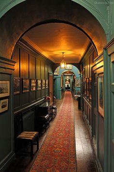 the hallway is lined with antique furniture and framed pictures on the walls, along with an ornate rug