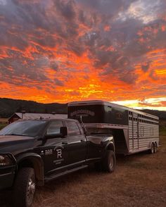 a truck with a trailer attached to it parked in a field under a colorful sky