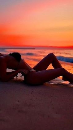 a woman is laying on the beach at sunset