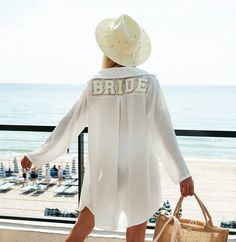 a woman in a white shirt and hat standing on a balcony looking out at the beach