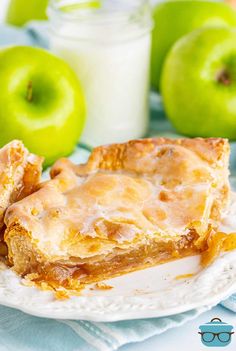 two pieces of apple pie on a white plate next to green apples and a glass of milk