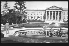 an old black and white photo of people walking in front of a building with columns