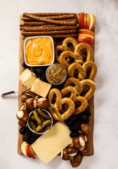 an assortment of pretzels, cheese and dips on a wooden cutting board