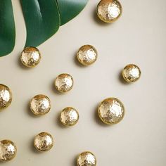 some gold colored beads are on a white surface next to a green leaf and plant