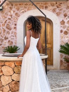 a woman standing in front of a stone wall wearing a white wedding dress with straps