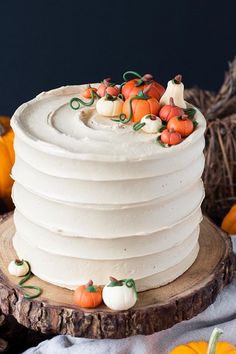 a white cake sitting on top of a wooden plate next to pumpkins and gourds