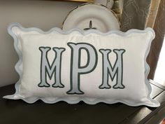 a decorative pillow with the letter m p m on it sitting on a table next to a clock