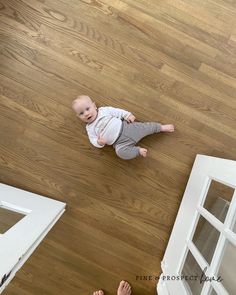 a baby sitting on the floor looking up at someone's feet in the air