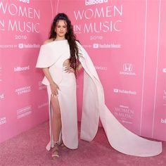 a woman wearing a white dress and cape standing in front of a pink carpeted wall