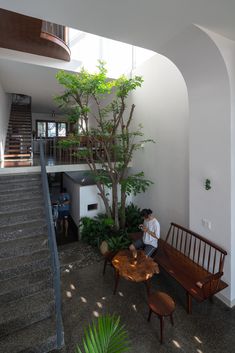 a man sitting on a bench next to a tree in a living room with stairs