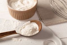 a wooden spoon filled with white powder next to a whisk on a plate