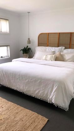 a bed with white linens and pillows in a bedroom next to a rug on the floor