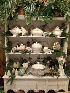 an old china cabinet is decorated with christmas greenery and white dishes on it's shelves