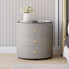 a round table with drawers and a vase on top in front of a striped wall