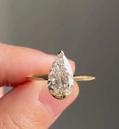 a woman's hand holding an engagement ring with a pear shaped diamond