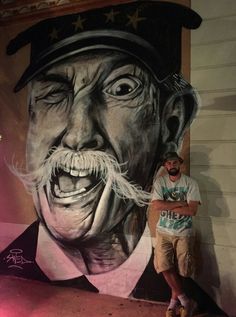 a man standing in front of a painting of a man with a mustache and moustache