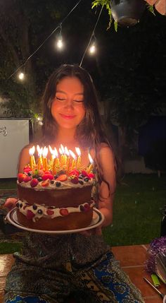 a woman sitting in front of a cake with lit candles