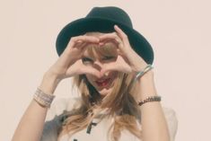 a woman wearing a white shirt and black hat holding her hands up to her face