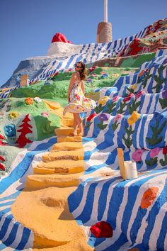 a woman standing on top of a colorful hill next to a tall white and blue building