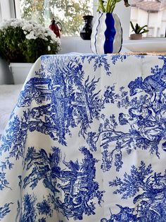 a blue and white table cloth with flowers in a vase on the table next to it