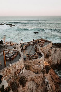 an outdoor dining area overlooking the ocean with tables and chairs set up on top of it