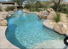 an outdoor swimming pool surrounded by rocks and cactus plants in the desert with a water feature