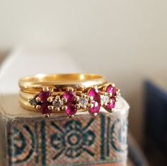 two gold rings with pink and white stones on top of each other in front of a box