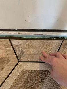 a person's hand is on the edge of a wood floor that has been stained white