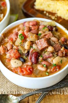 two white bowls filled with beans and sausage soup next to a piece of bread on a wooden table