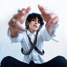 a man in white shirt and black tie sitting on the floor with his hands up