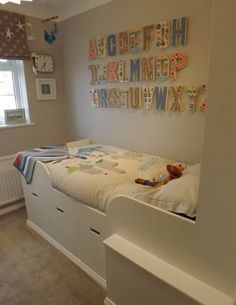 a child's bedroom with white furniture and letters on the wall above the bed