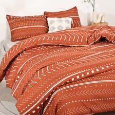 a bed with an orange and white patterned comforter set on top of the bed