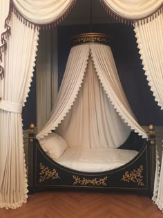 a canopy bed with white drapes and pillows on it's sides in a room