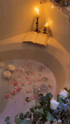 a bathtub filled with flowers and candles next to a book on top of it